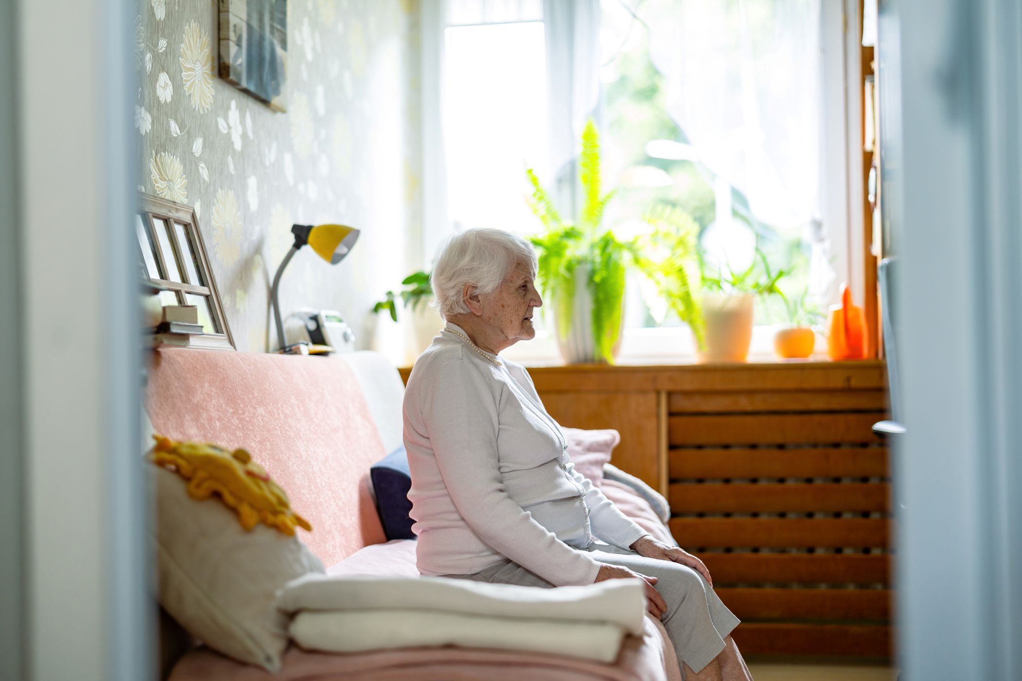 Senior woman with dementia sits alone on sofa staring ahead.
